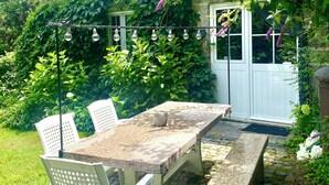 A patio with a stone table and chairs, surrounded by greenery and a white fence. - QUINTA DE RIBAS - LE VERGER - SMALL CHARMING GITE (vila cha do marao, amarante)