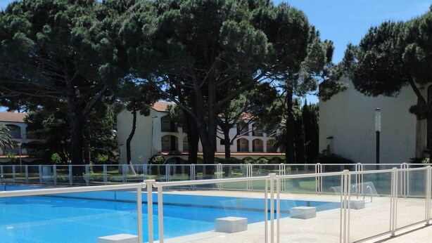 Una piscina con recinzione bianca, circondata da alberi e un edificio con tetto in tegole.