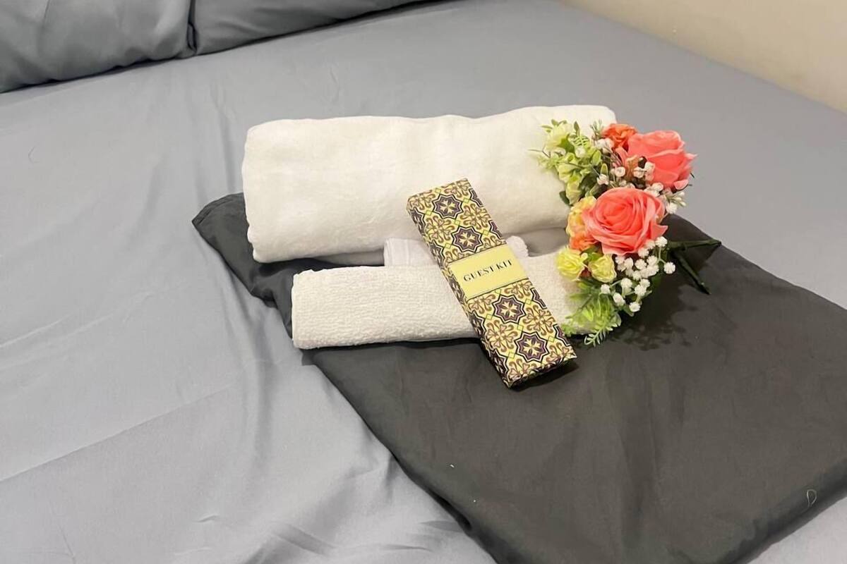 A neatly made bed with a grey sheet, a white towel, a black pillow, and a floral arrangement.