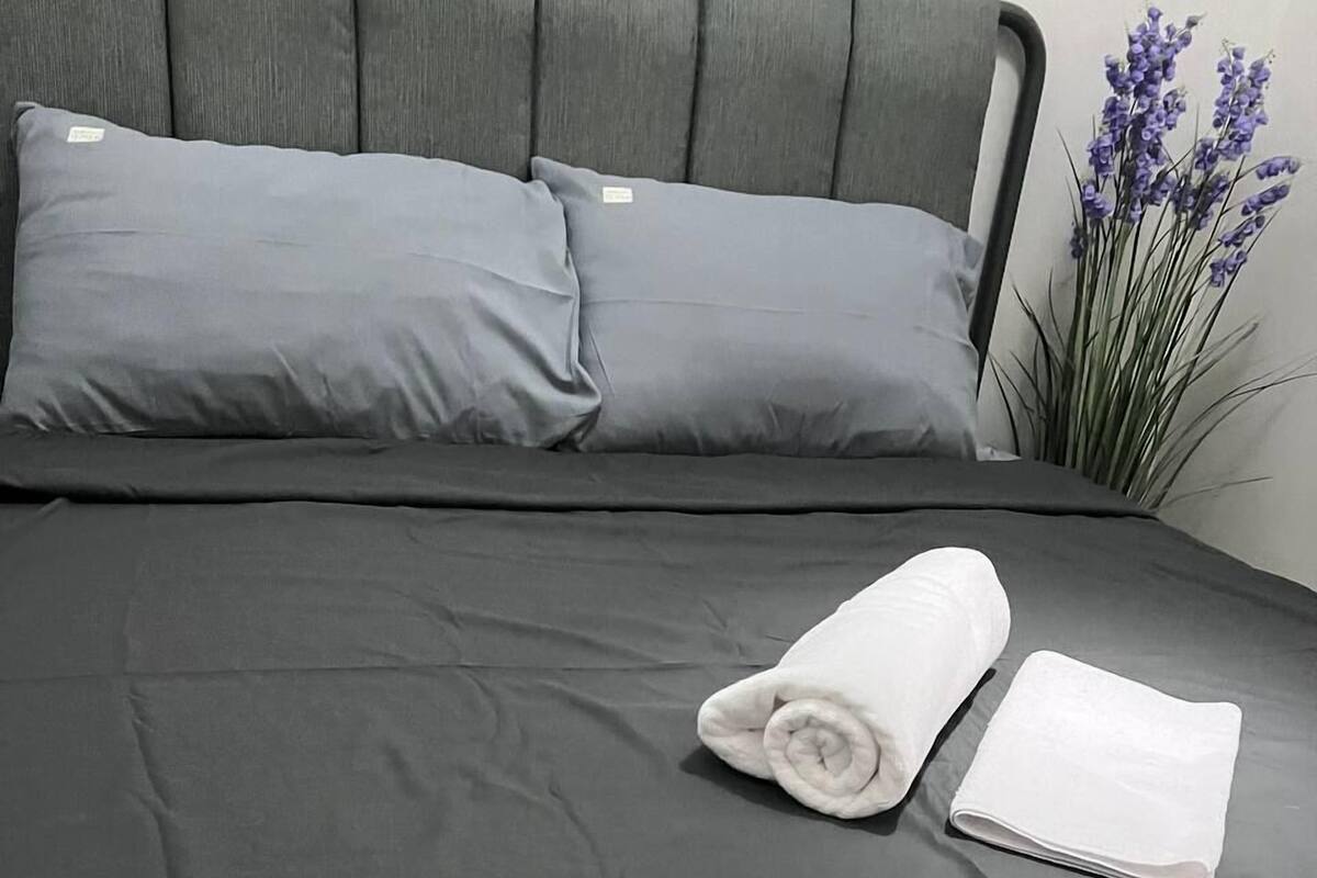 A neatly made bed with grey bedding and two rolled white towels.