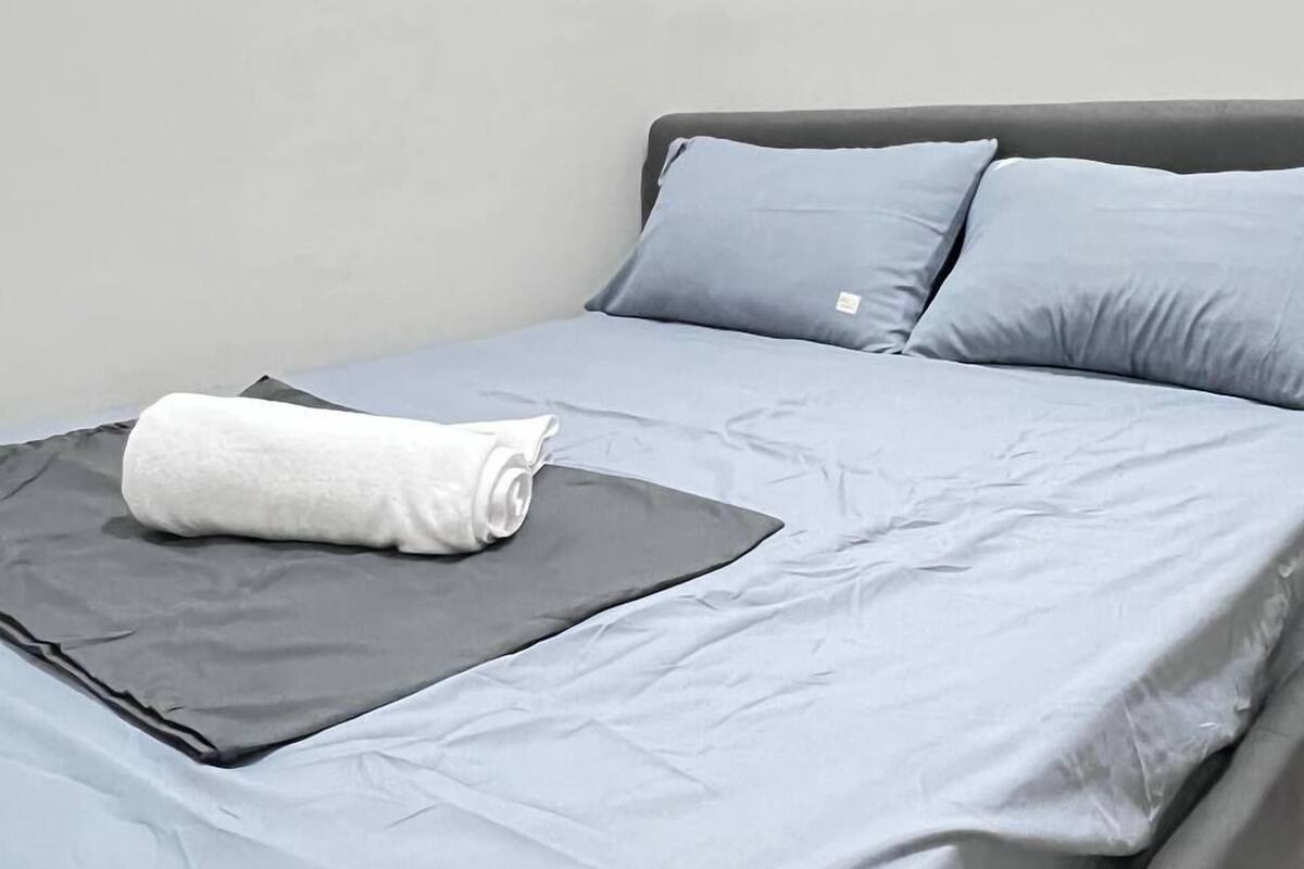 A bed with grey bedding and a white towel, a grey pillow, and a grey headboard.