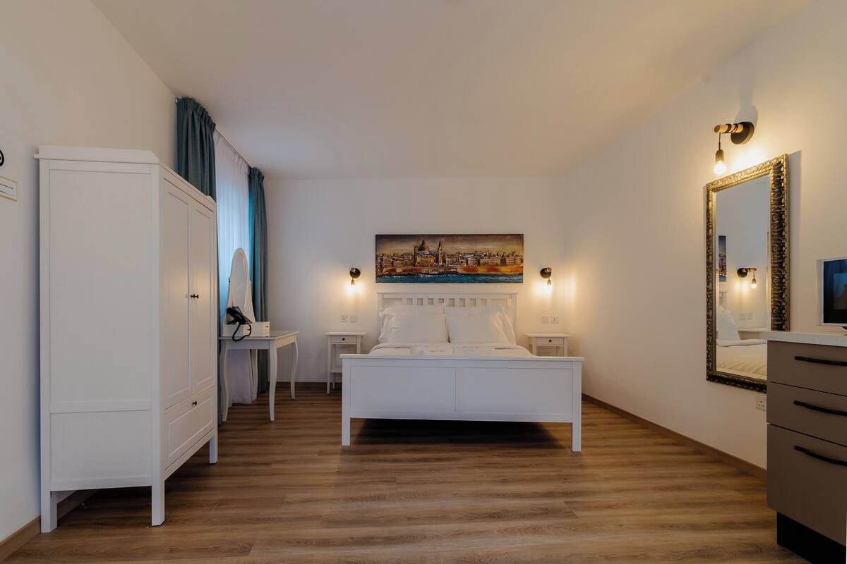 Un dormitorio con una cama blanca, un cuadro sobre la cama y un espejo en la pared.