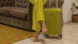 Una mujer sentada en un sofá marrón con una maleta verde a su lado.