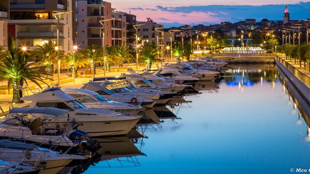 A marina with boats docked, a bridge, and buildings in the background.