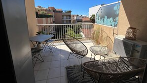 A balcony with a table, chairs, and a small air conditioning unit.