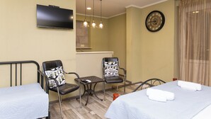 Une chambre d’hôtel avec deux lits, une télévision, une horloge et une petite table avec des chaises.