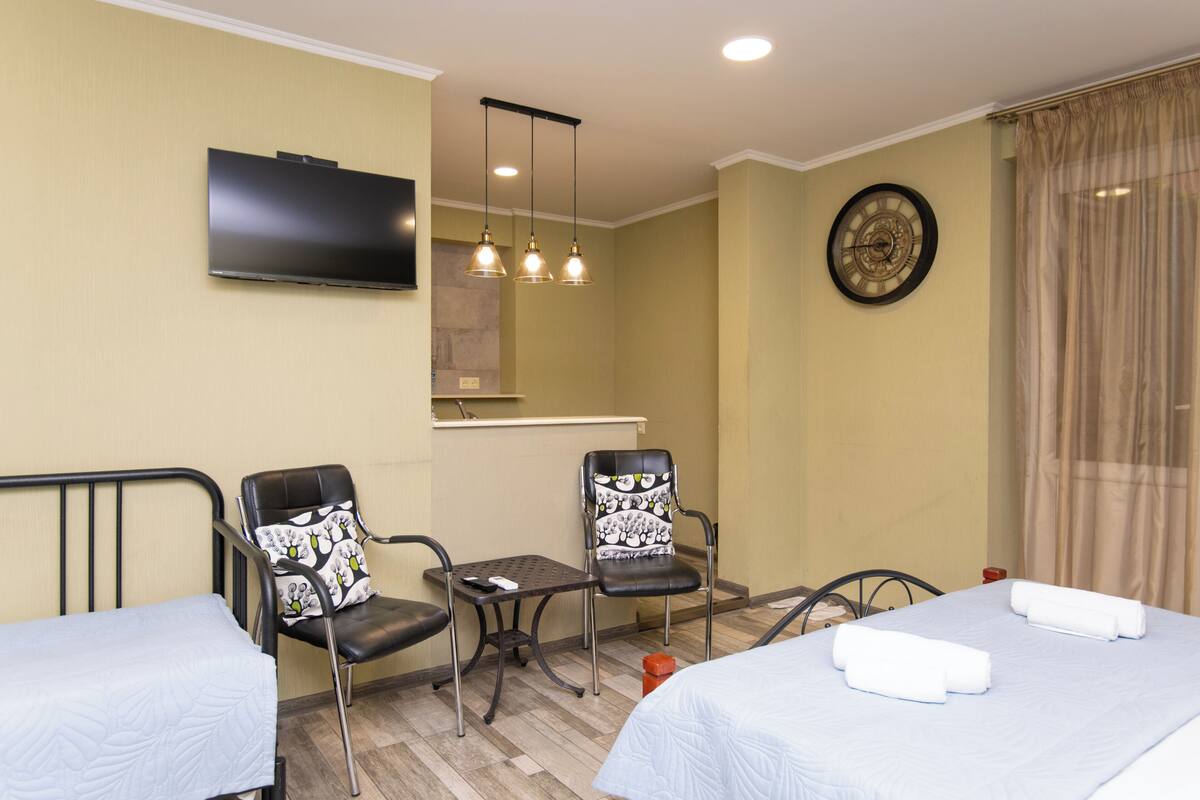 Une chambre d’hôtel avec deux lits, une télévision, une horloge et une petite table avec des chaises.