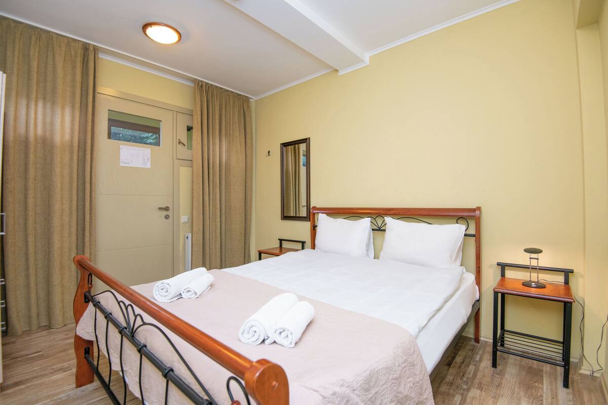 Une chambre d’hôtel avec un lit en bois, une table de chevet, une commode et un miroir au mur.