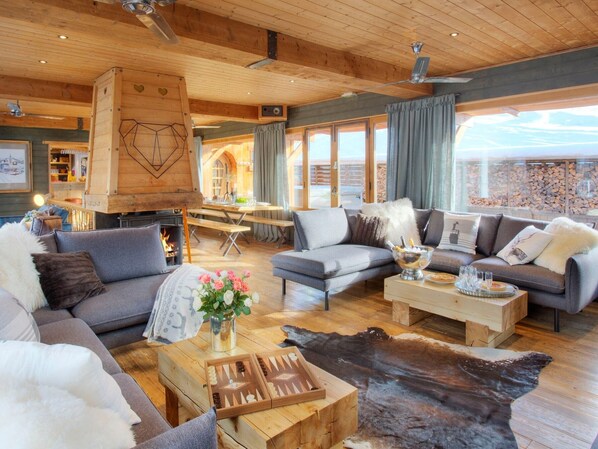 A cozy interior with a fireplace, sofas, a dining table, and a view of the outside.