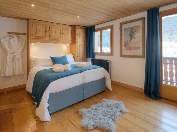 Un dormitorio con cama, armarios de madera, radiador, un cuadro enmarco y ventana con cortinas.