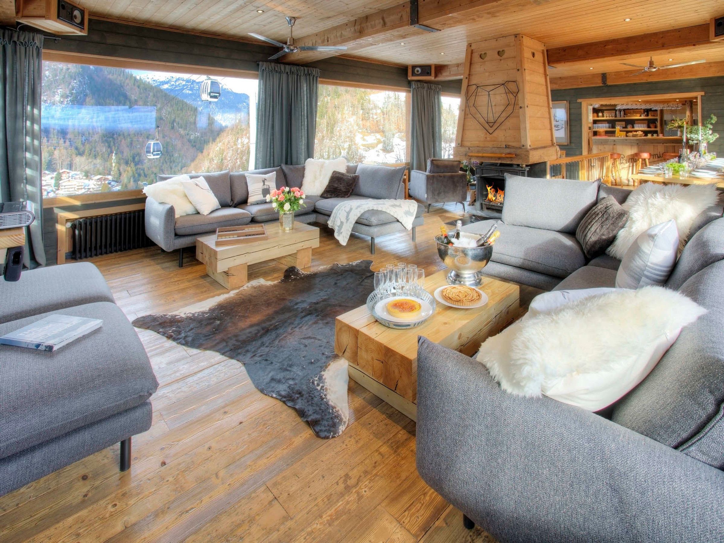 A cozy living room with a large window, a fireplace, and a rustic wooden ceiling.