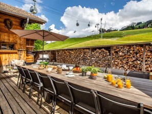 An outdoor dining area with a wooden table, chairs, and a grill.