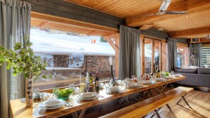 A long wooden dining table set for a meal, with a bench in the middle, large windows, and a view of a snowy landscape. - 5☆ Chalet, 15 ppl, spa, pet-friendly, La Clusaz (La Clusaz)