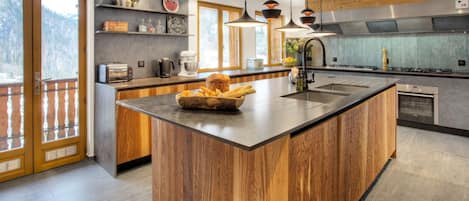 Una cocina moderna con una isla grande de madera, electrodomésticos de acero inoxidable y vistas al exterior.