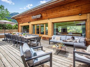 A wooden deck with outdoor seating, a dining area, and large windows offering a view of the surrounding landscape.