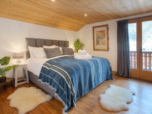 Un dormitorio con cama, mesita de noche, lámpara, planta, cuadro enmarcado y balcón con vistas.