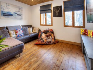 Un salón acogedor con un sofá de cuero, cojines estampados, suelo de madera y un ventanal con vistas a árboles.