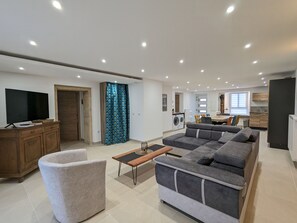 Ein modernes Wohnzimmer mit einem grauen Ecksofa, einem kleinen runden Couchtisch und einem Fernseher auf einer Holzkommode.