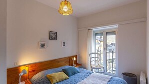 A bedroom with a bed, bedside lamps, a window with a view, and a hanging light fixture.