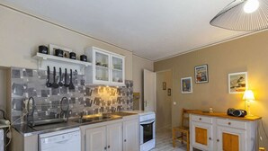 A compact kitchen with white cabinets, a tiled backsplash, a dishwasher, a stove, and a wooden dining table with chairs.