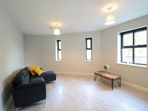 A spacious living room with a dark sofa, two windows, a wooden coffee table, and a hanging light fixture. - Charming 2-bed Apartment in Dublin's Countryside (Ballyboghil)