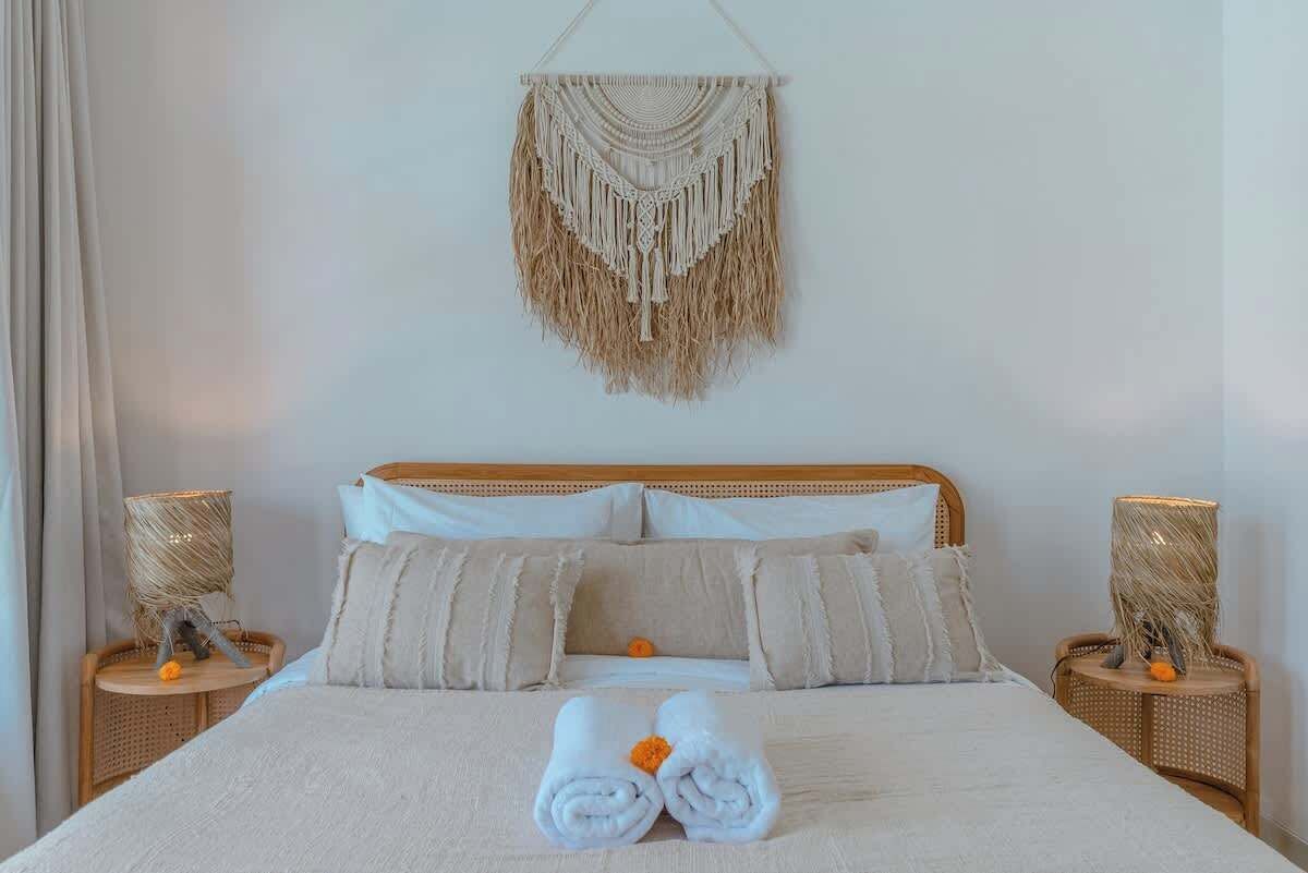 A neatly made bed with a macrame wall hanging above it, two bedside lamps, and a woven lamp on each side of the bed.