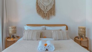 Un lit bien fait, avec une décoration murale en macramé au-dessus, deux lampes de chevet et une lampe en osier de chaque côté du lit.