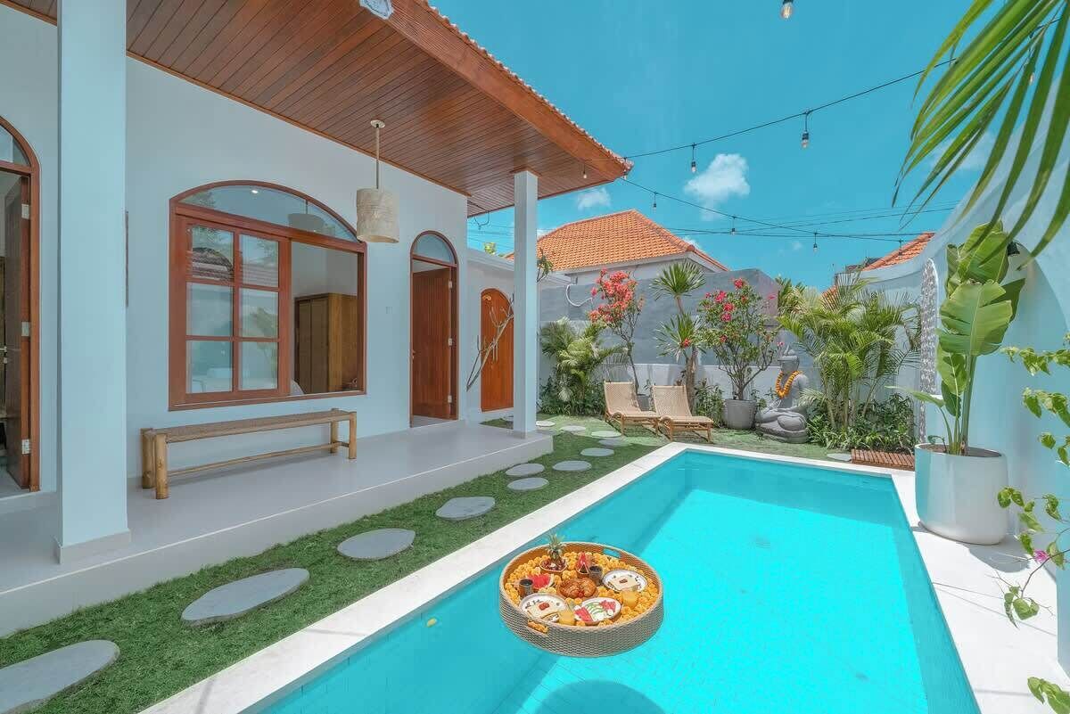 A modern house with a swimming pool, a wooden deck, and a garden with tropical plants.