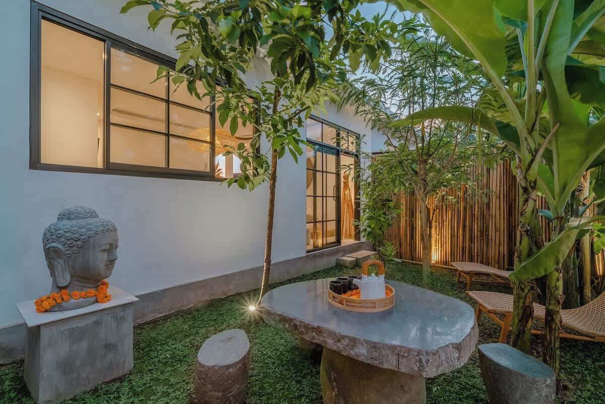 A serene outdoor area with a stone table, a Buddha statue, and a bamboo fence.