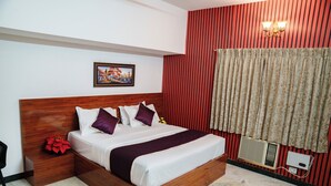 A neatly made bed with a wooden headboard, a nightstand with a red flower, and a wall-mounted air conditioning unit. - Rich Inn Palace Tnagar  (Chennai)
