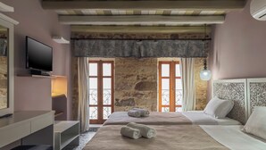 A hotel room with two beds, a TV, a desk, and a stone wall. - Vetus Oppidum Guesthouse (Chania)