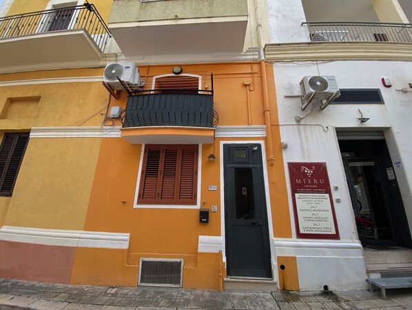 Stylish two-story building with a black door and two balconies, offering wine, olive oil, and artisanal products.
