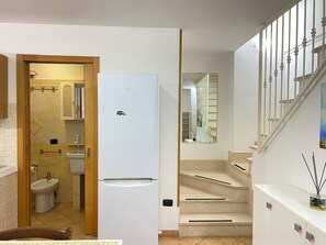 Spacious living area with a large refrigerator, bathroom with sink and toilet, and staircase leading to an upper floor.