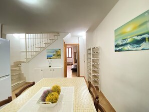 Enjoy meals in this elegant dining area with a high ceiling, featuring a dining table, shelving unit, and a beautiful seascape painting.