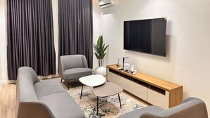 A modern living room with a sofa, armchair, coffee table, and a TV mounted on the wall. - La Crique Apartment (Abuja)