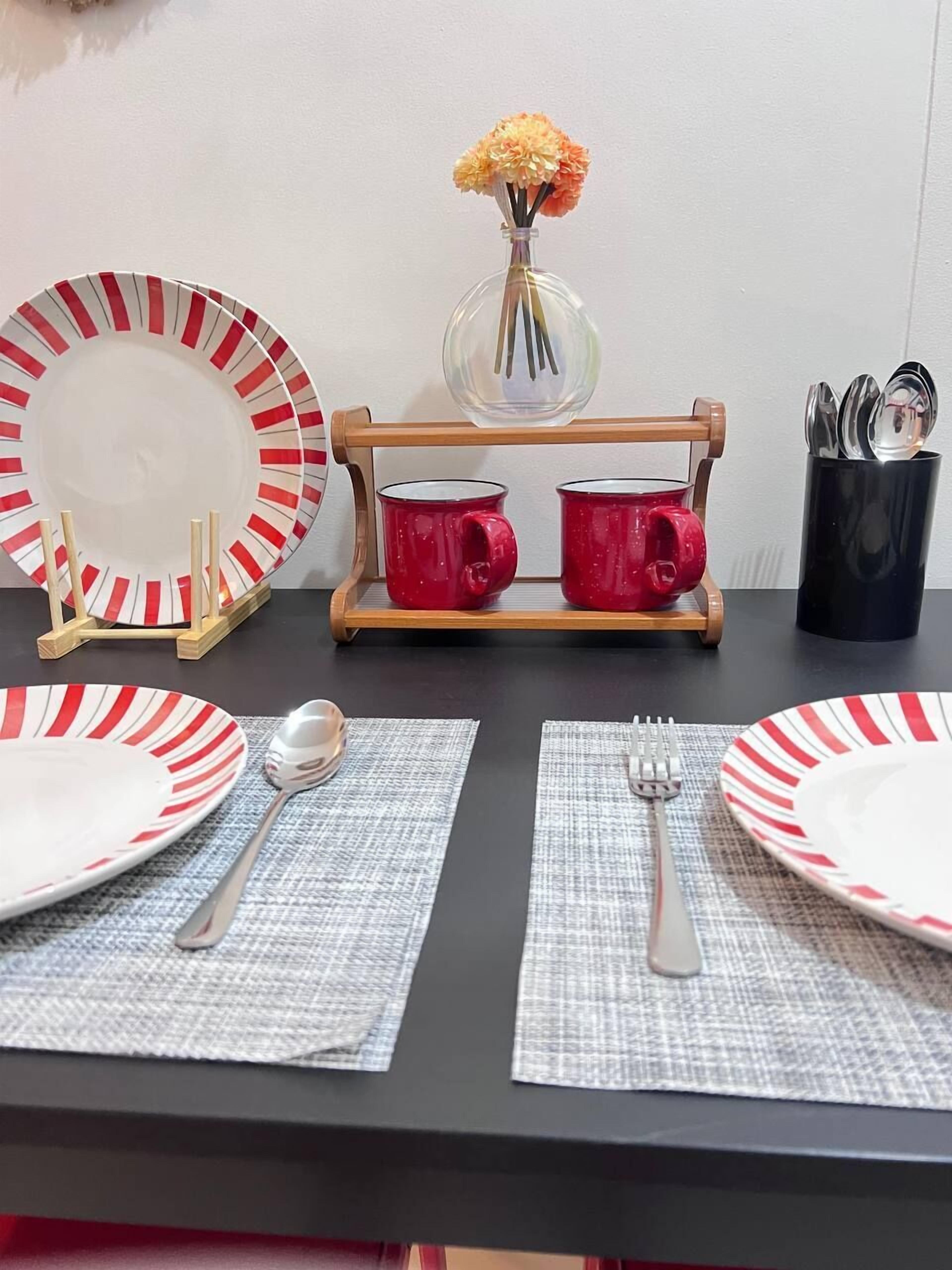 A dining table set with striped plates, red mugs, and a vase with flowers.