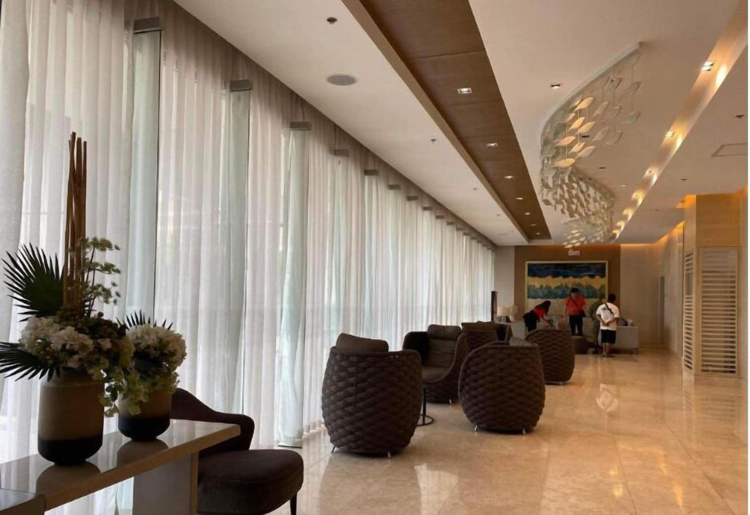 Un hall d’entrée moderne avec un long comptoir de réception, des sièges confortables et une grande fenêtre agrémentée de rideaux légers.