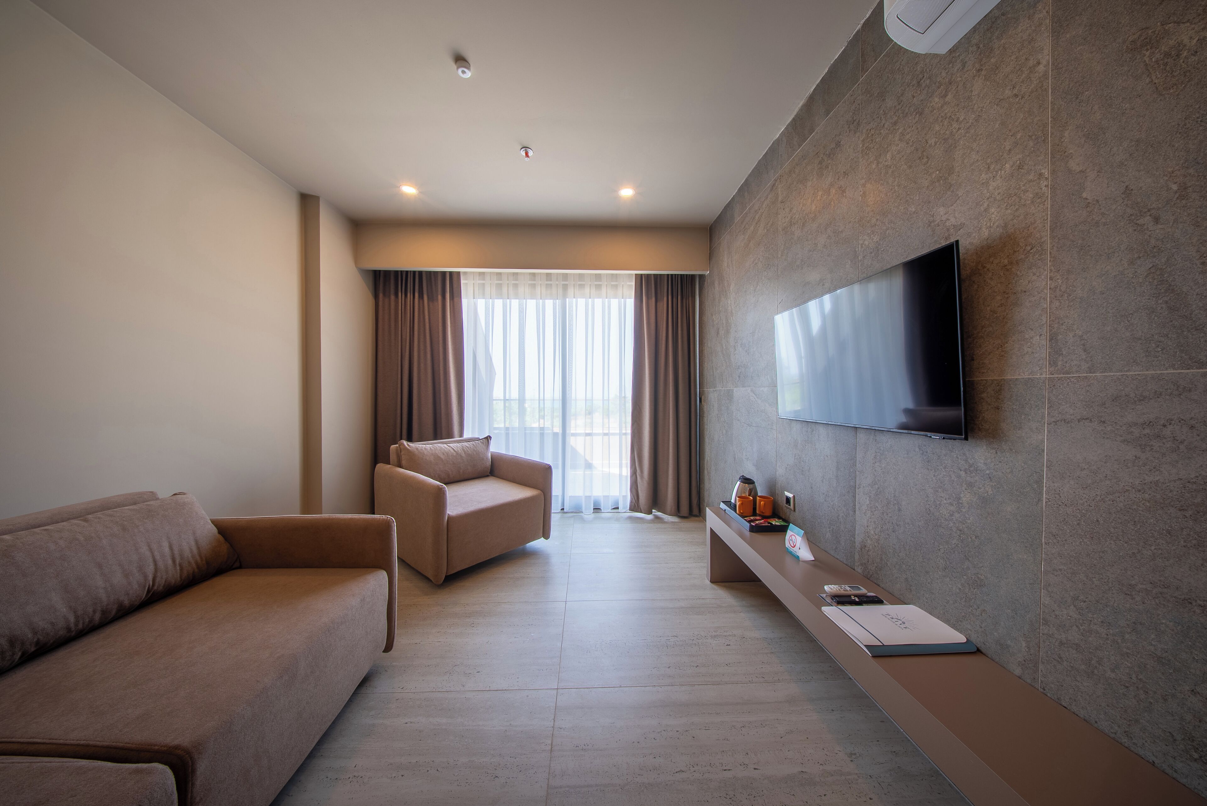 Un salon moderne comprenant un canapé, un fauteuil, un téléviseur à écran plat fixé au mur et une petite table avec un plateau.