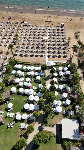 An aerial view of a beach resort with rows of sunbeds and umbrellas, a central pathway, and a beach in the background. - Prive Suite Side & Spa Hotel Adults Only 16 Plus (Manavgat)