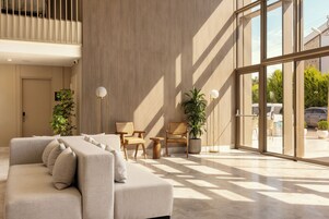 A modern lobby with a sofa, chairs, potted plants, and large windows.