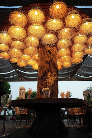 A tree-shaped light fixture with multiple spherical lights, a wooden table, and wicker chairs. - Prive Suite Side & Spa Hotel Adults Only 16 Plus (Manavgat)