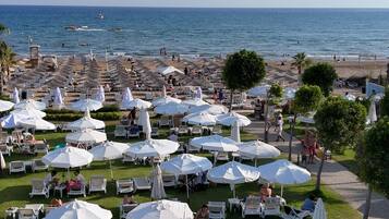 Un resort frente a la playa con numerosas tumbonas blancas y sombrillas, vista despejada al océano y una zona de césped bien cuidada.