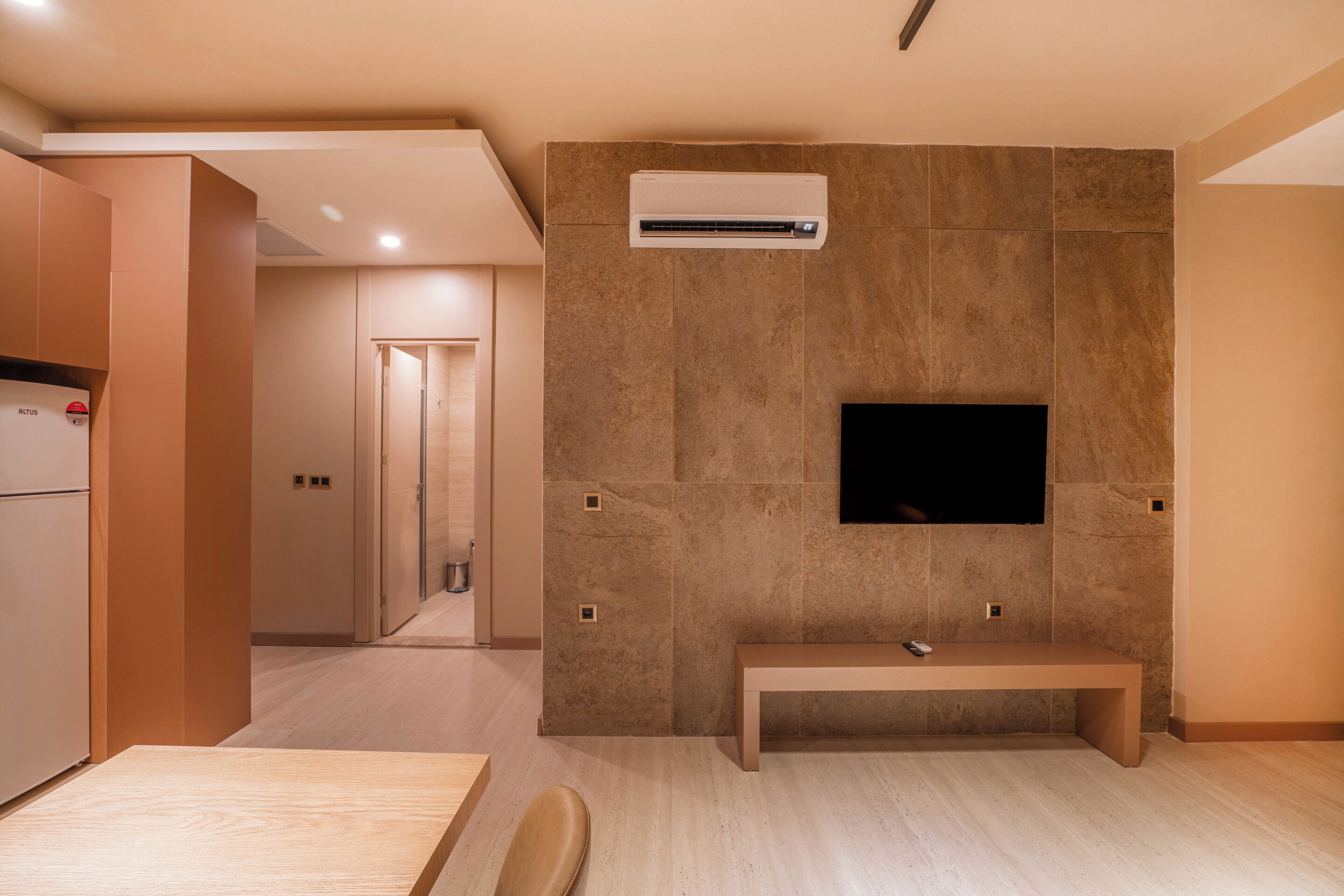 A modern kitchen with a built-in oven, a bench, and a flat-screen TV mounted on a stone wall.