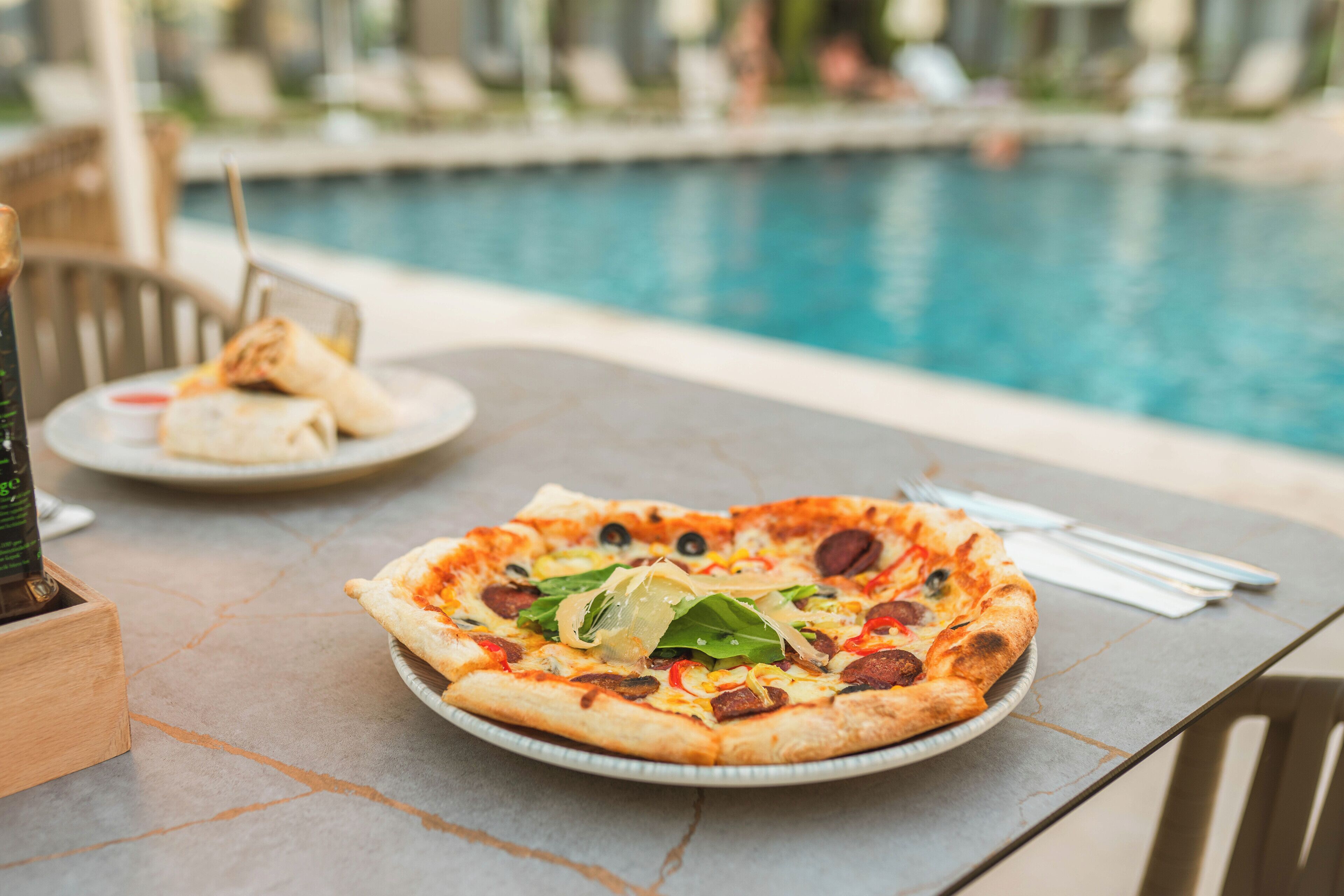 Eine Pizza auf einem Tisch in der Nähe eines Schwimmbeckens.