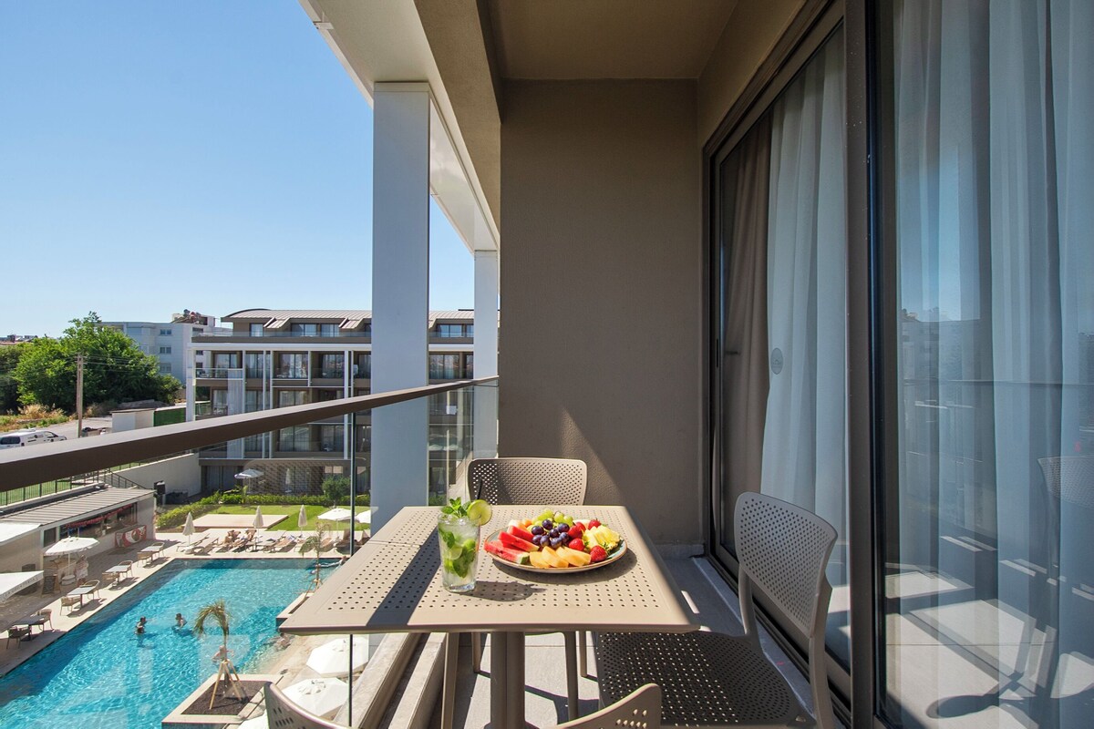 A balcony with a pool, a table with fruit and a drink, and a chair.
