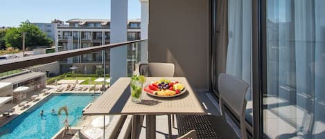 A balcony with a pool, a table with fruit and a drink, and a chair.