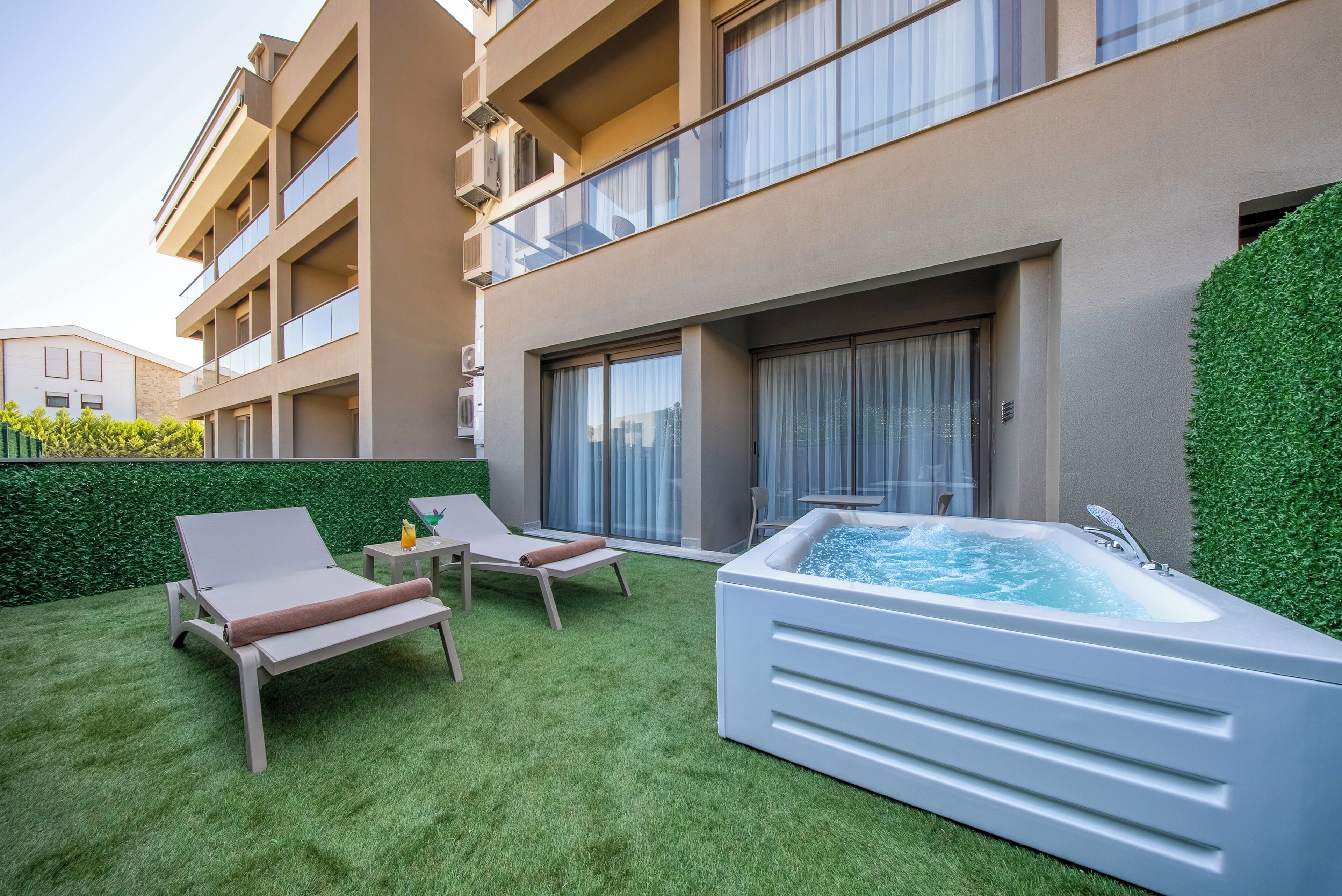 A modern outdoor area with a hot tub, two lounge chairs, and a well-maintained lawn.