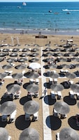 A beach with numerous umbrellas and sun loungers, a wooden walkway, and a sign reading 'COPPA French Riviera Club'.
