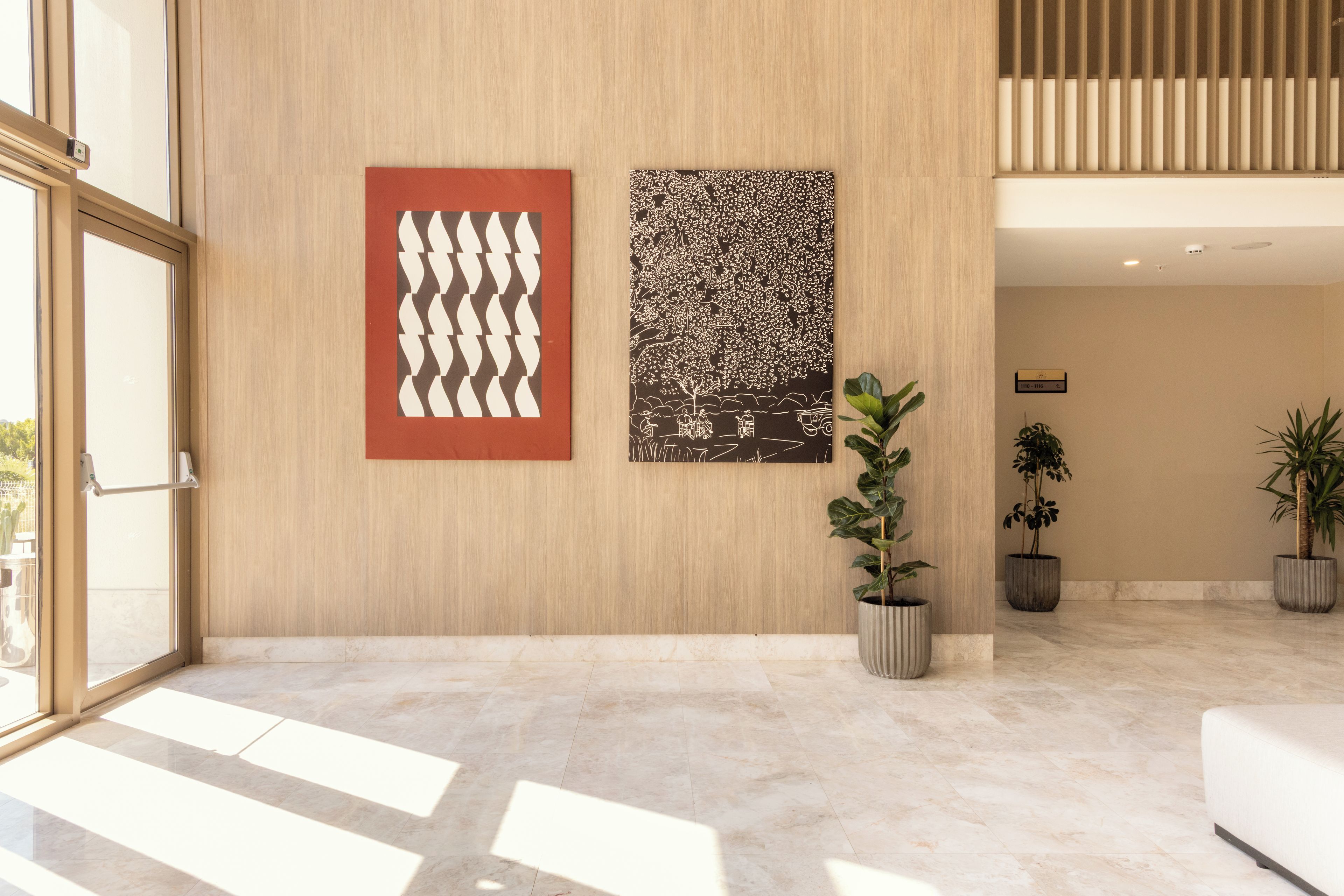 A modern interior with a wooden wall, two abstract artworks, and a potted plant.