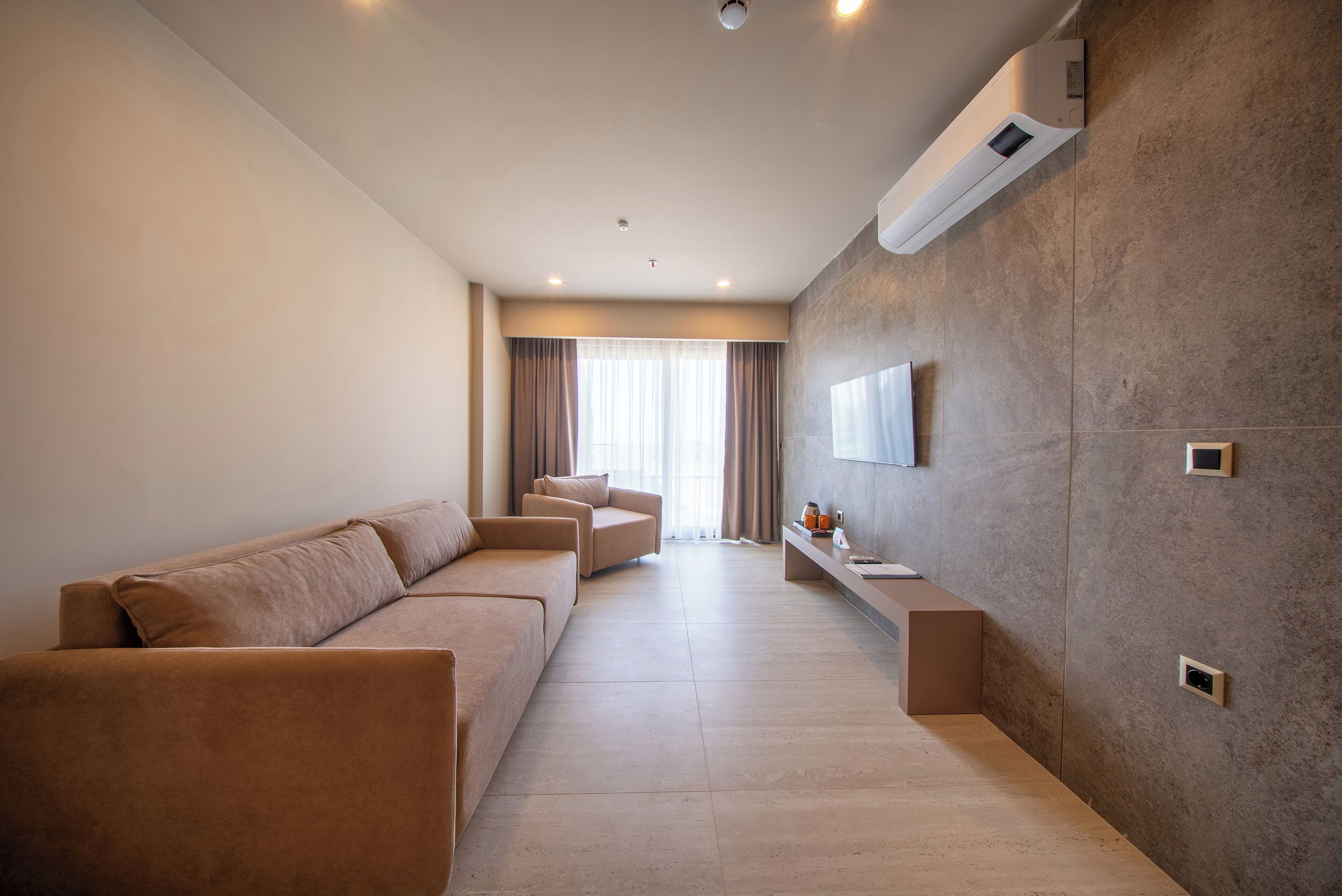 Uma sala de estar moderna com sofás, uma TV de tela plana na parede e um ar-condicionado instalado.